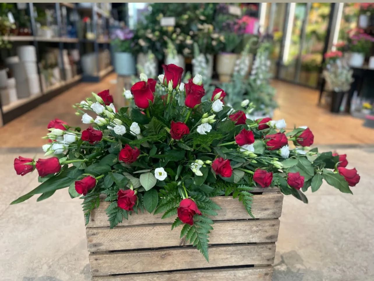Kistdekoration med röda rosor och vita blommor - begravningsbinderi Stockholm.
